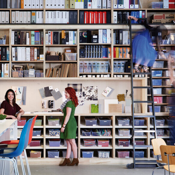 Creative office space with women discussing design materials and a ladder for shelf access.
