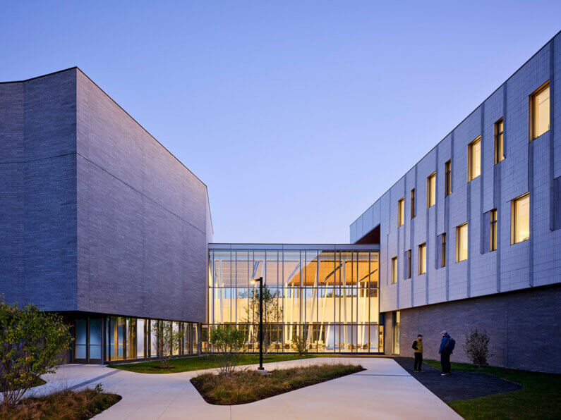 Modern architecture featuring a glass walkway between two buildings at dusk.