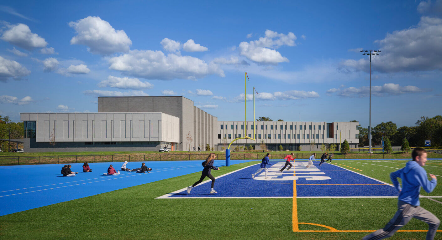 Students exercising on a blue athletic field with a modern school building in the background.