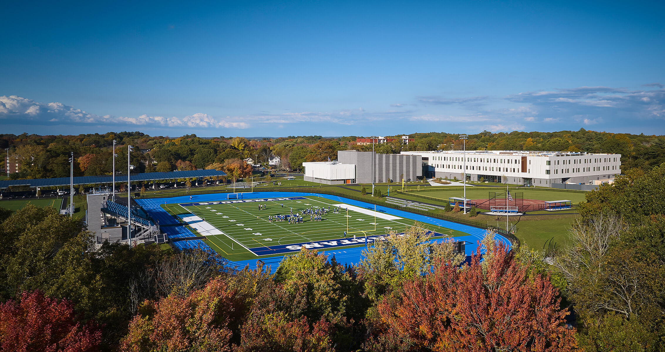 Aerial view of a sports field with players and modern school buildings nearby.