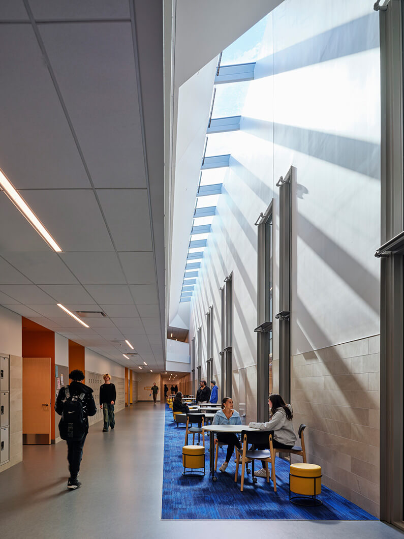 Bright, modern school hallway with students studying and collaborating at tables.