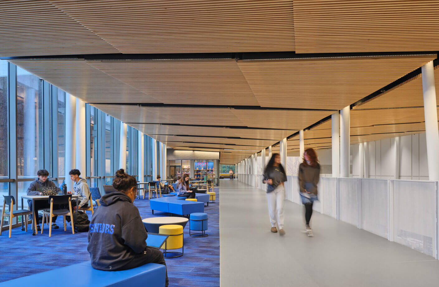 Modern study space with students working and walking in a bright, open hallway.