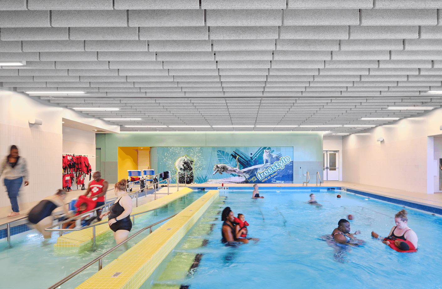 Indoor swimming pool with families enjoying water activities and colorful murals.