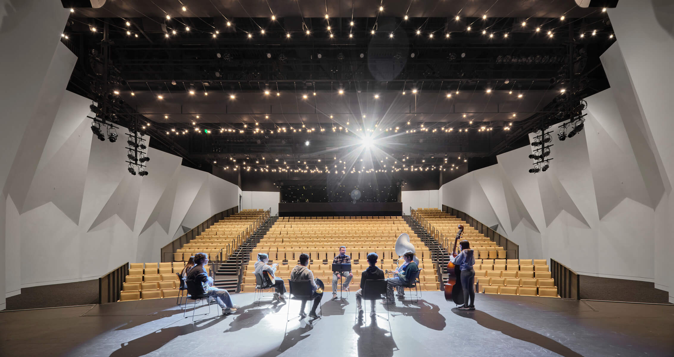 Rehearsal in a modern auditorium with musicians on stage and empty seating.