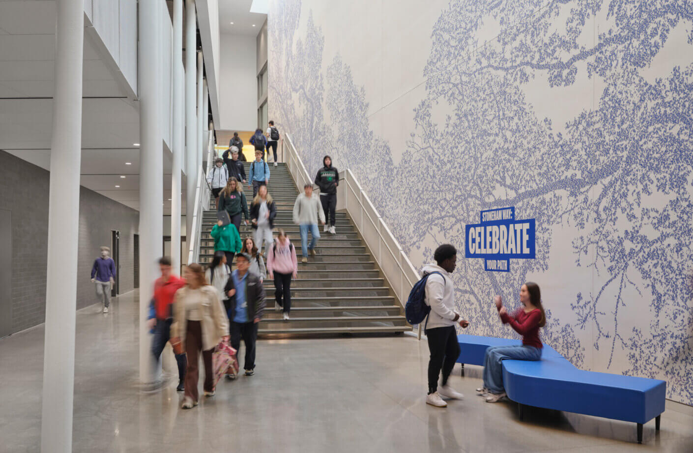 Students walk through a modern building with a mural and a Celebrate Your Path sign.