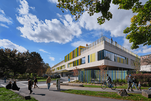 The William E. Carter School featuring a colorful facade, surrounded by people and greenery on a sunny fall day.