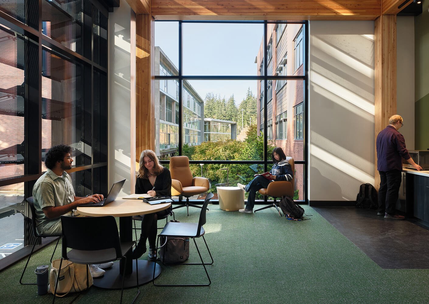 Modern study space with students collaborating by large windows and greenery outside.