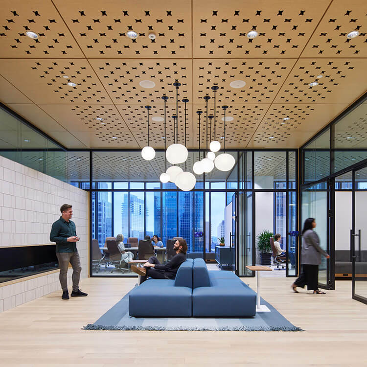 Modern office interior with glass walls, stylish furniture, and people engaged in conversation.