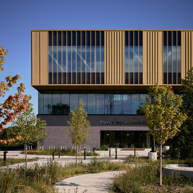 Entrance of Rouge Valley Community Centre showcasing large windows, slatted gold paneling, and landscaped greenery in front.