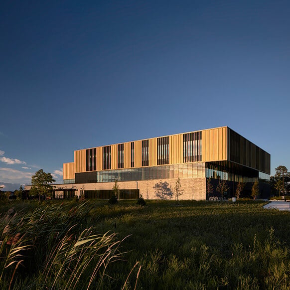 Architectural building with large glass windows, set against a blue sky and green landscape.