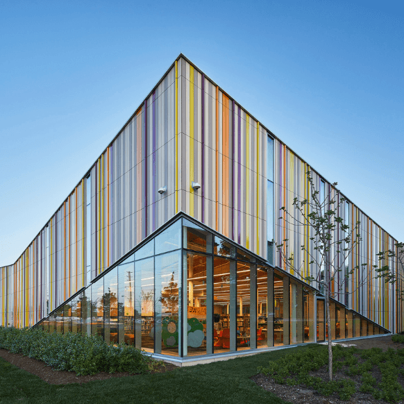 Colorful modern building with angular design and large windows, surrounded by greenery.