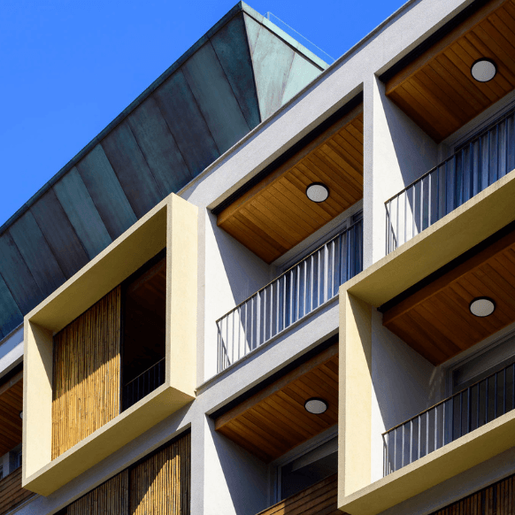Modern apartment building façade with wooden balconies and blue sky backdrop.