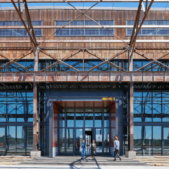 Modern industrial building facade with large glass entrance and visitors outdoors.