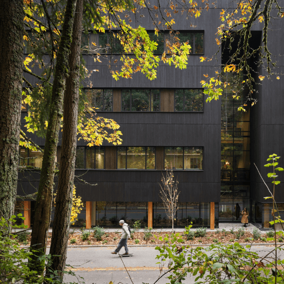 Modern building amid autumn foliage with pedestrians walking on a tree-lined street.