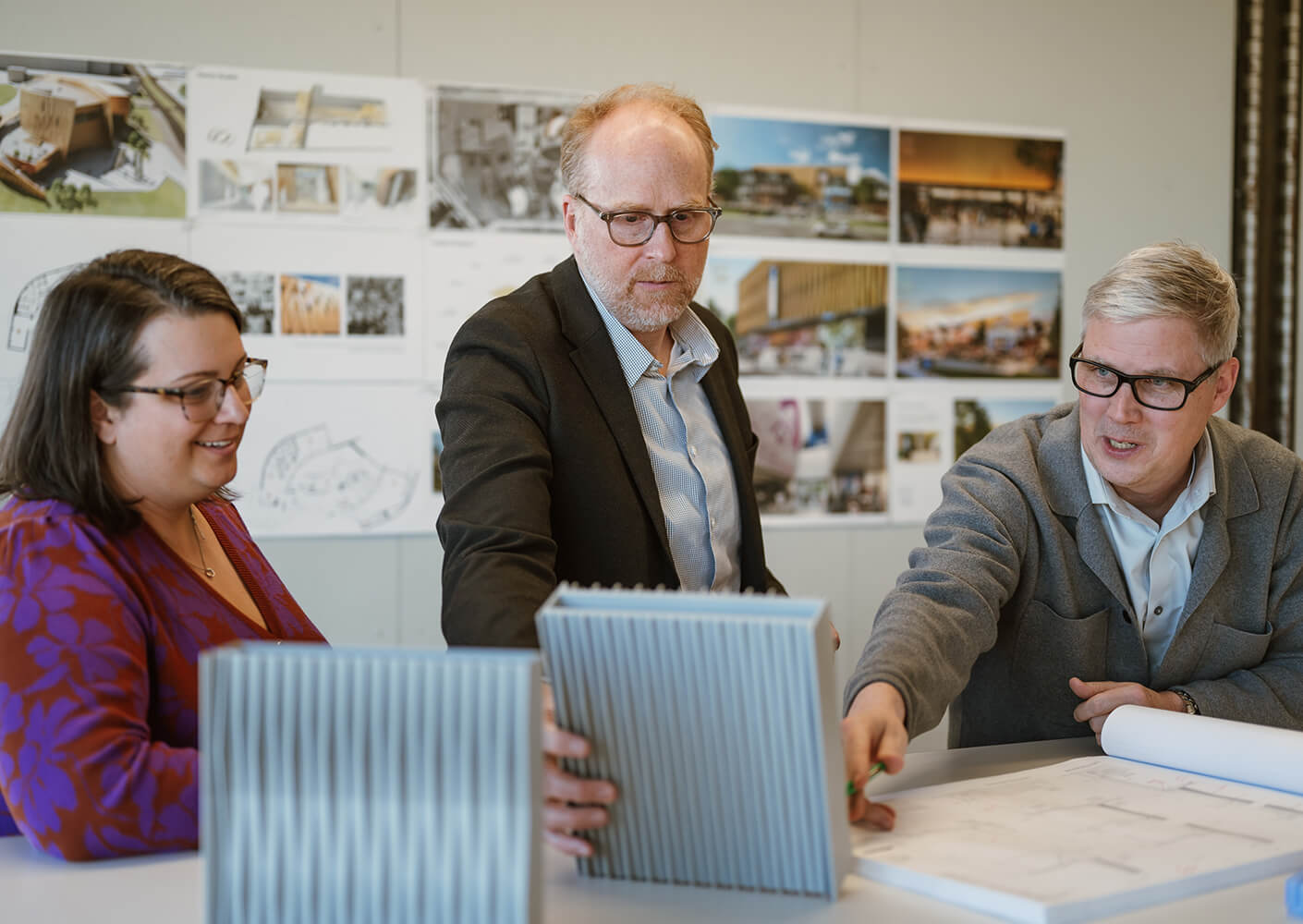 Three professionals collaborate on architectural designs at a table with models and plans.