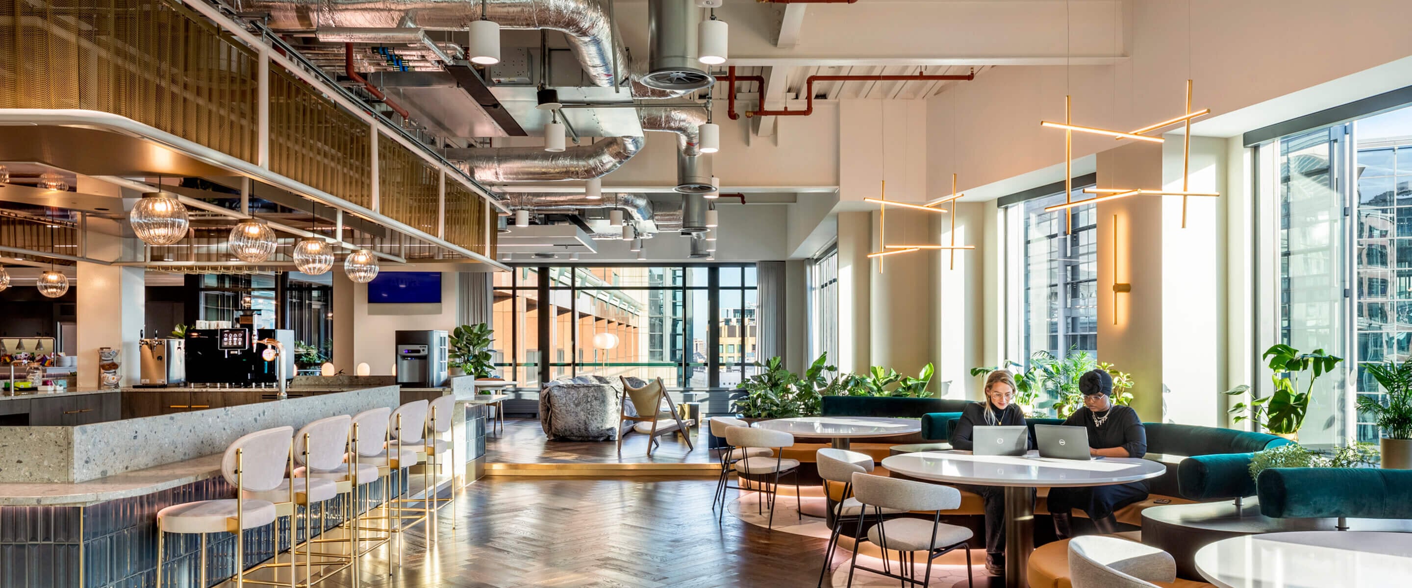 Bright open space featuring sleek lines, industrial elements, and varied seating arrangements, complemented by large windows and a herringbone wood floor.