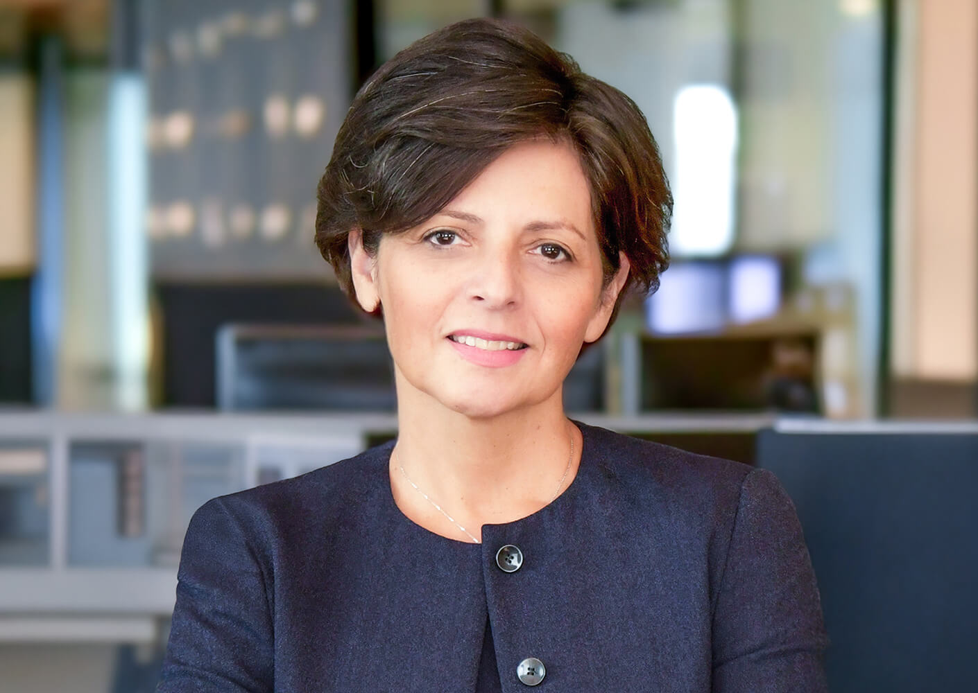 Confident professional woman with short hair, posed in a modern office setting.
