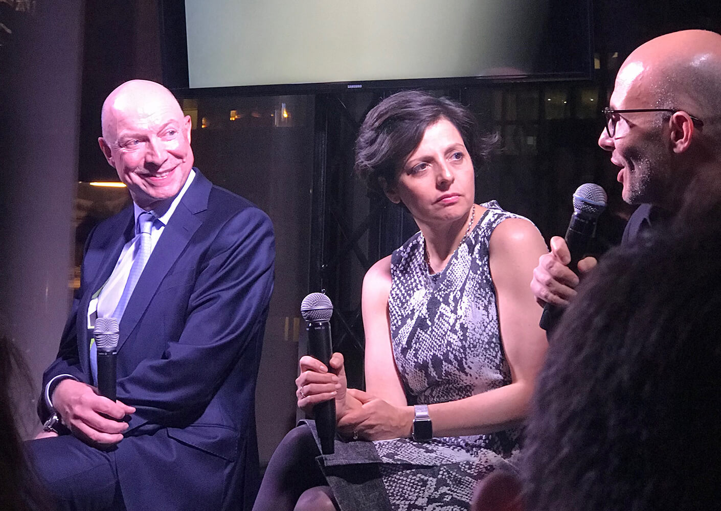 Panel discussion with three speakers, one man smiling and two others engaged in conversation.