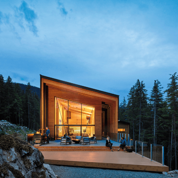 Modern wooden cabin with stunning architecture surrounded by forest at dusk.