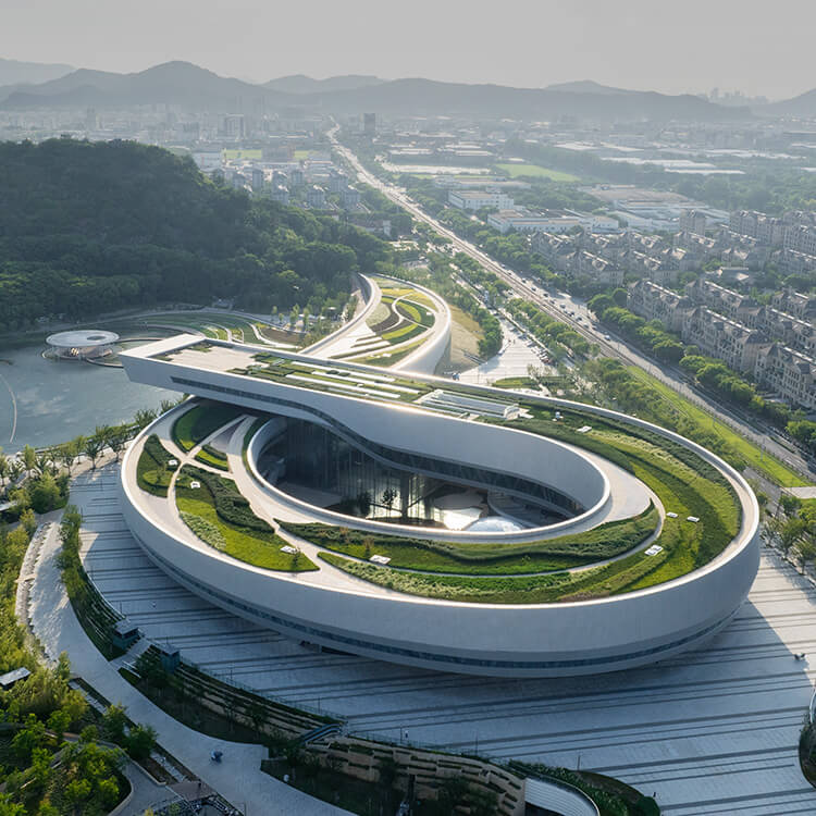 Aerial view of the ribbon-shaped Suzhou Museum of Science and Technology surrounded by green landscapes and cityscape.