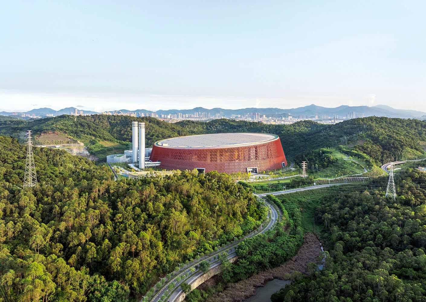 Aerial view of a modern power station surrounded by lush greenery and mountains.