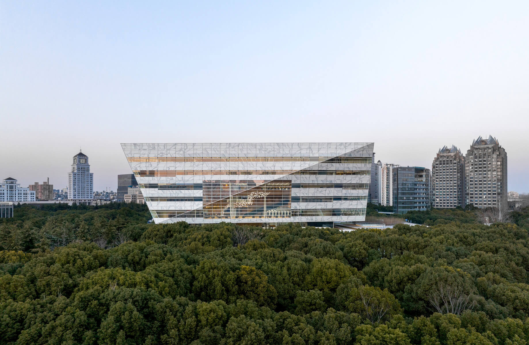 Modern glass building amidst greenery and urban skyline. Architectural design in focus.