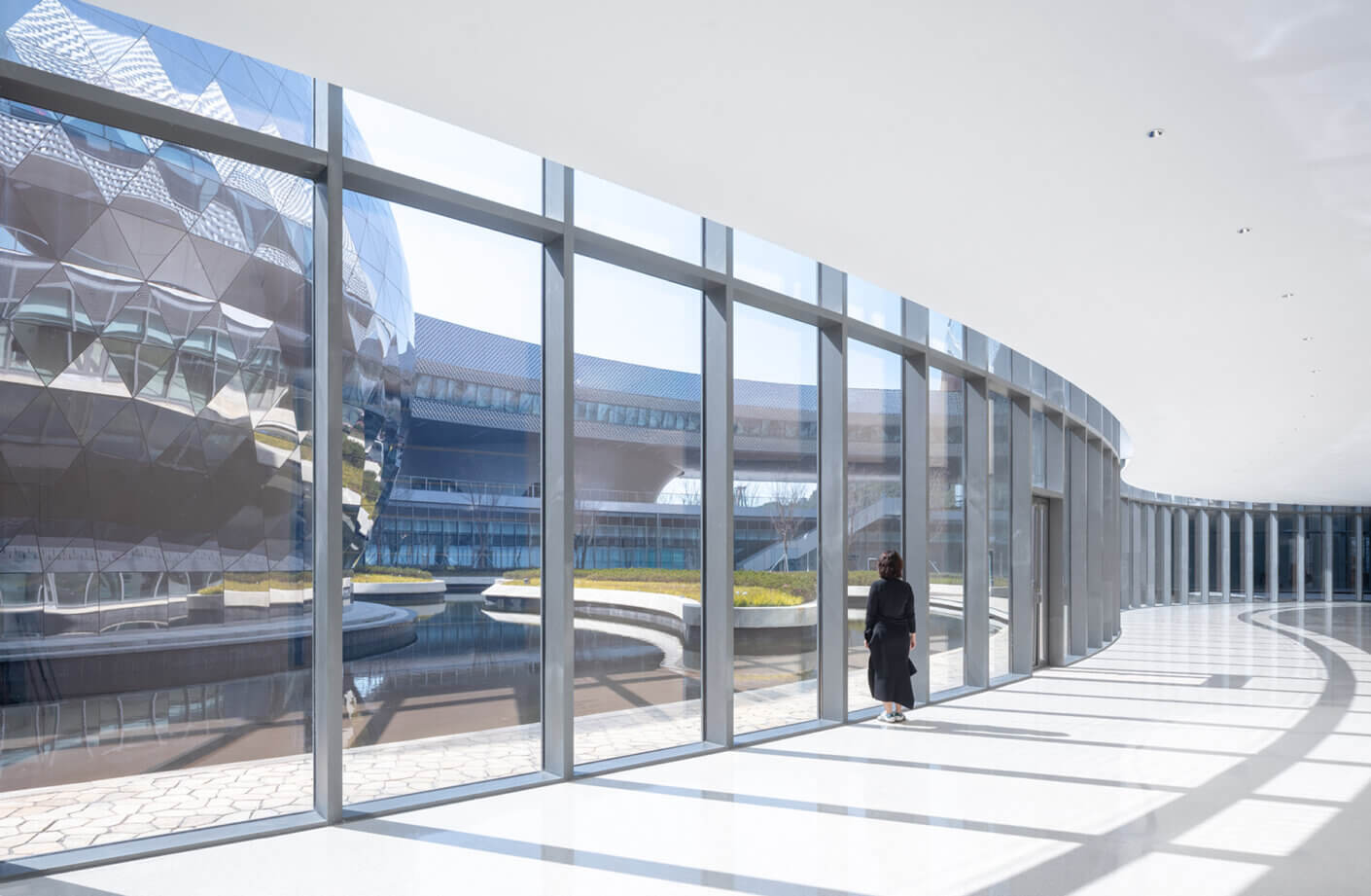 Modern interior with large windows, sleek design, and a person admiring the courtyard view outside.