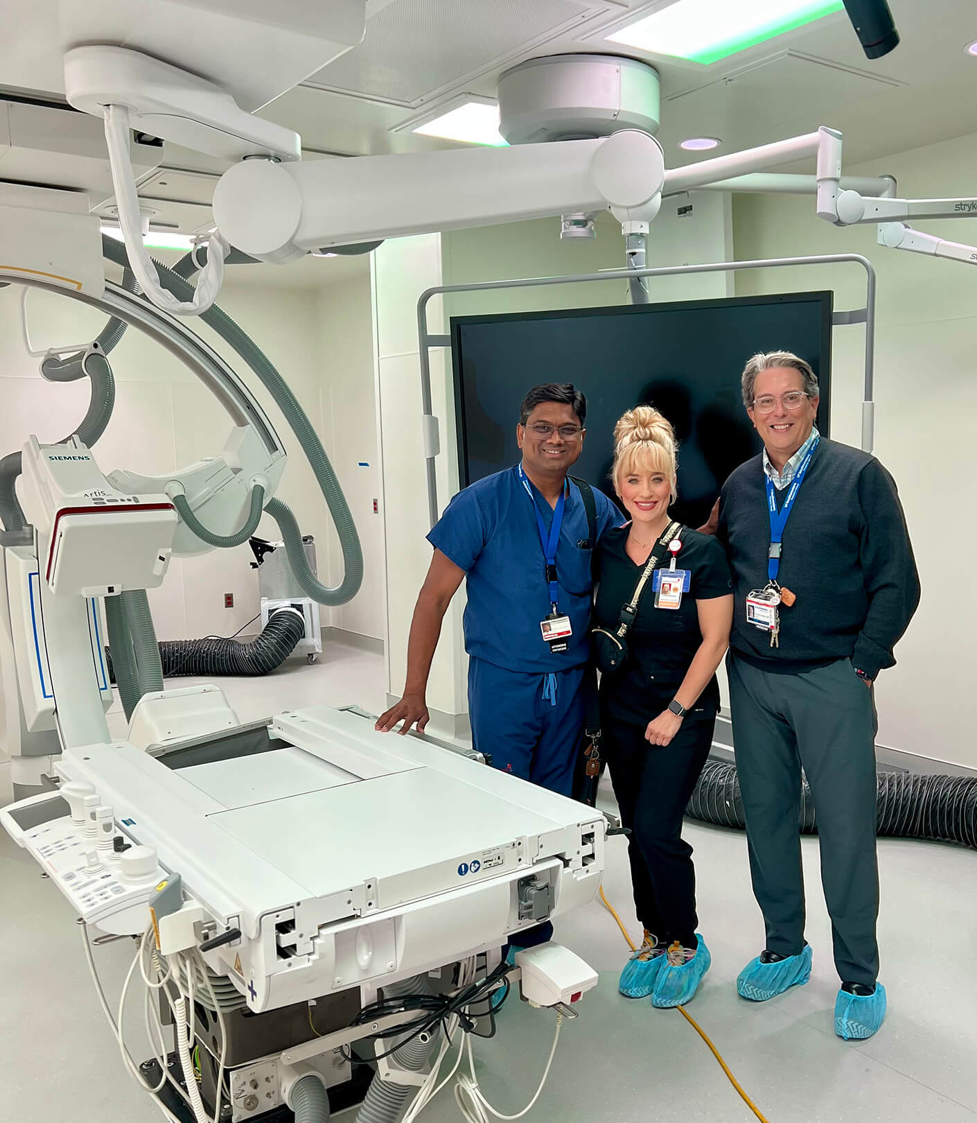 Andrea and two healthcare professionals pose in a modern medical room with advanced equipment.
