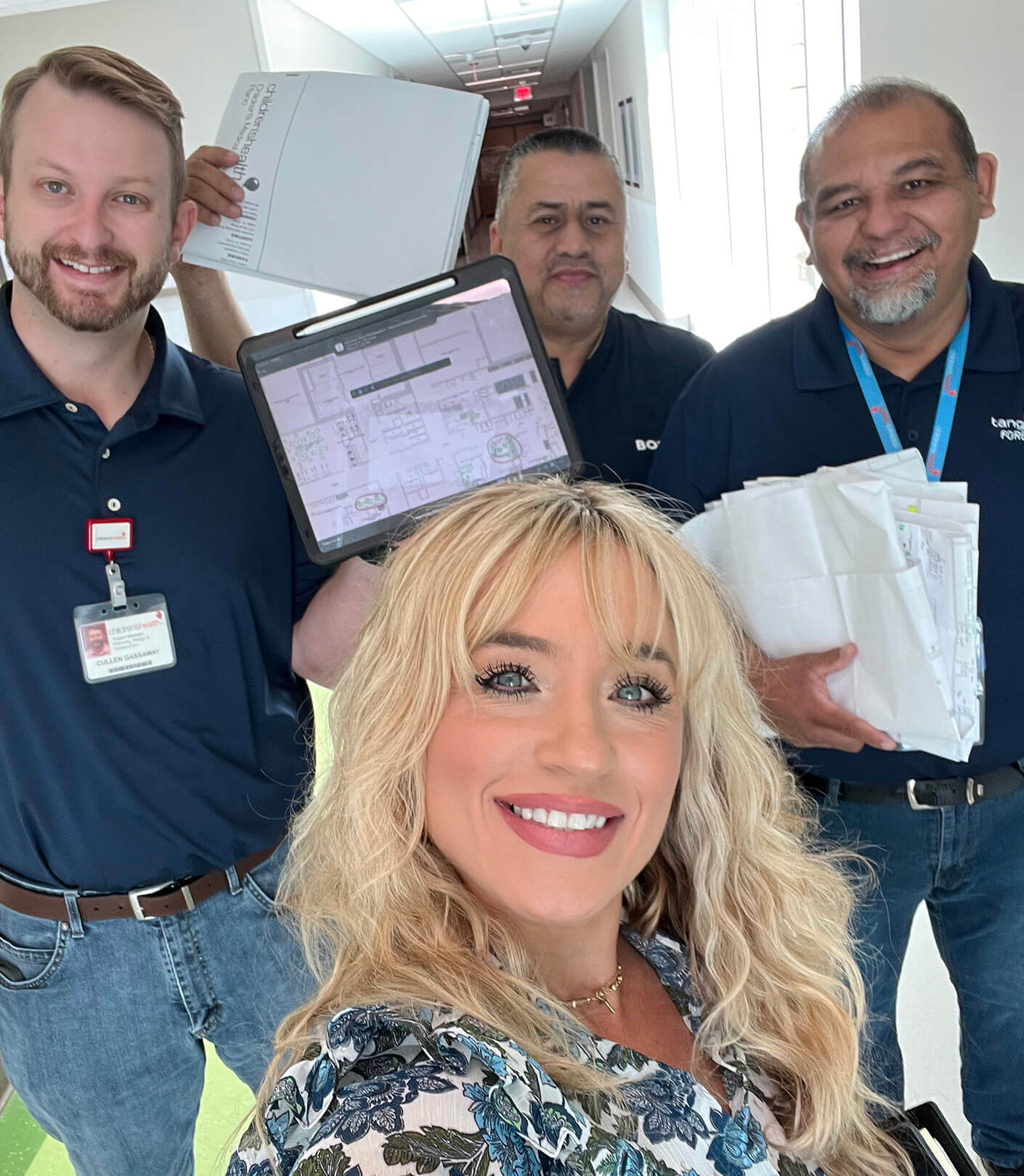 Team celebrating success in a hallway, holding documents and devices. Smiles all around!