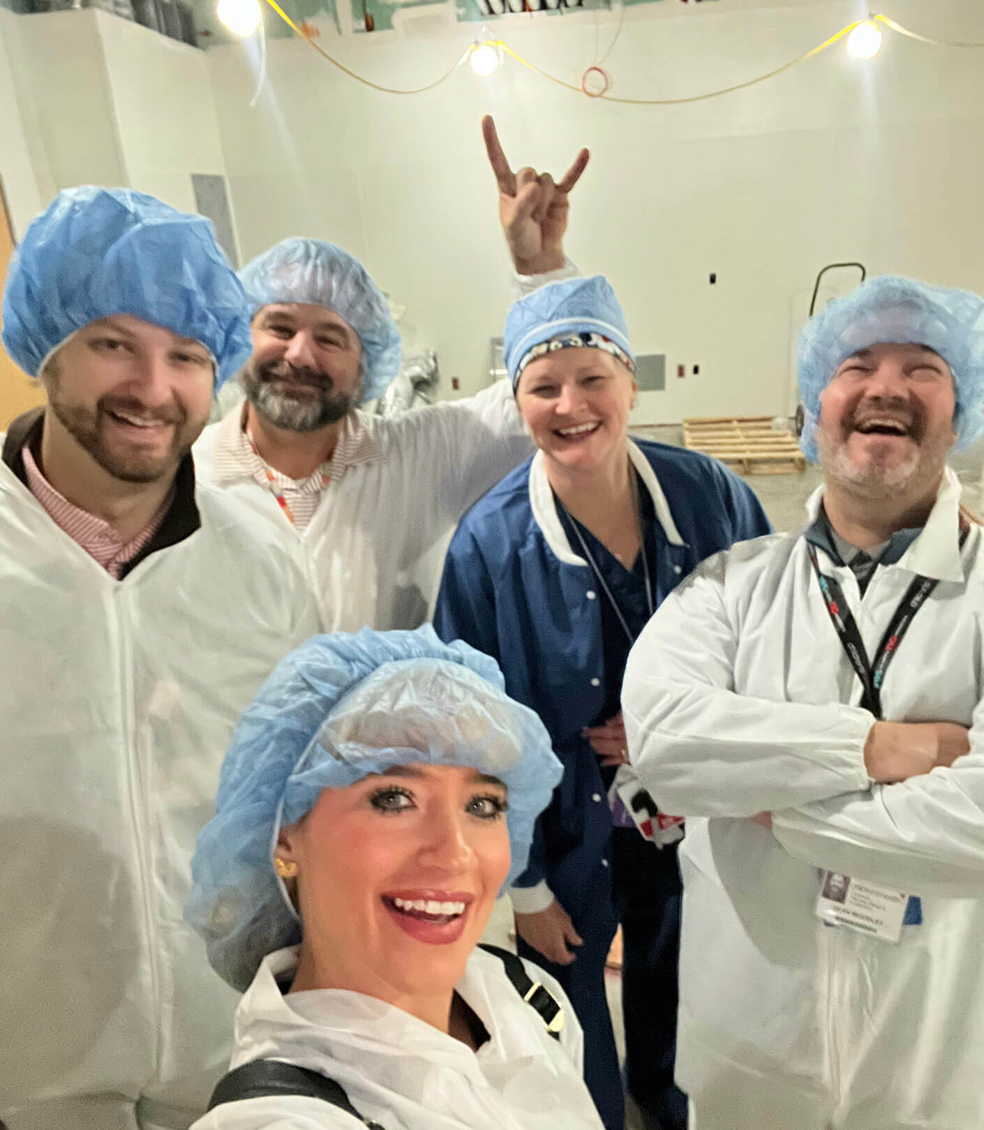 Andrea with team in safety gear smiling for a selfie in a cleanroom environment.