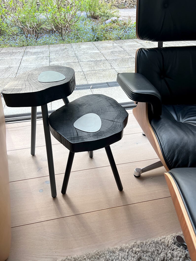 Stylish black wooden side tables with inlaid designs near a modern chair and garden view.