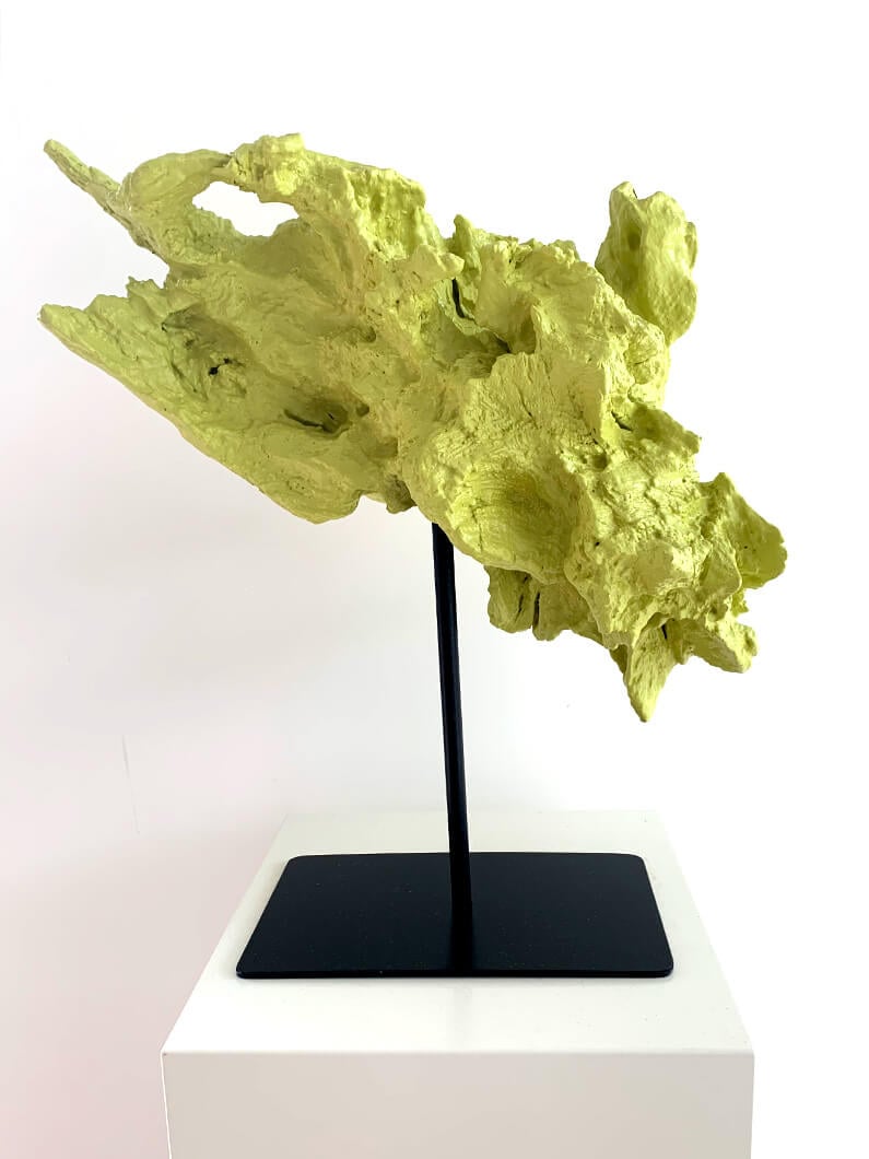 Abstract green sculpture displayed on a stand against a white background.