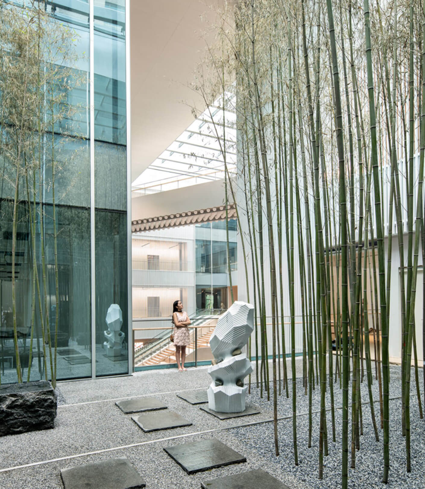 Interior view featuring vertical bamboo installations, stone pathways, and a sculptural element amidst glass and stone architecture.