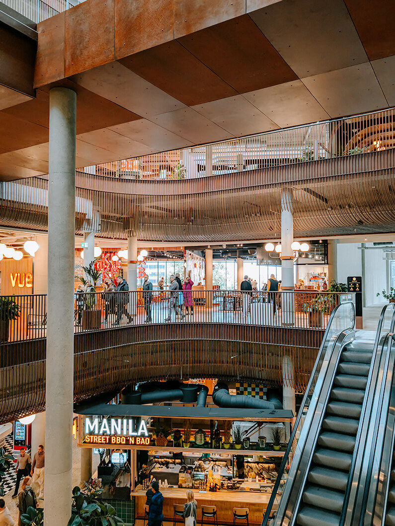 Modern interior of a bustling food hall with multiple levels and eateries.