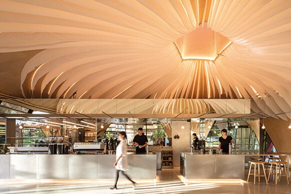 Interior view of a café featuring a sculptural ceiling design with layered shapes, reflective surfaces, and open space creating a unique atmosphere.