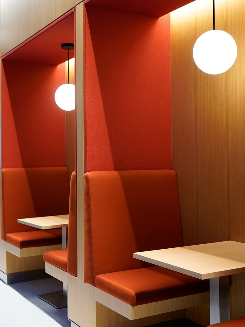Seating area with red upholstered booths, wooden accents, and pendant lighting. Minimalist design for a cafe or restaurant setting.