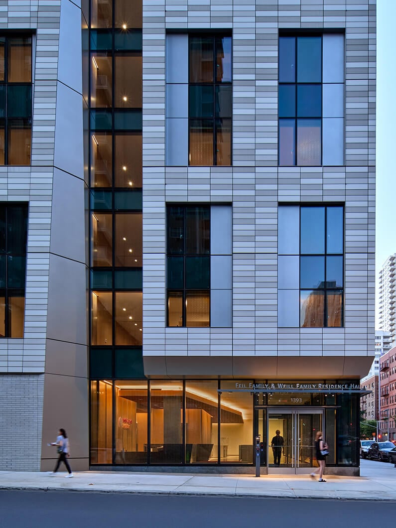 Exterior view of the Feil Family & Weill Family Residence Hall, featuring large glass windows and contemporary architectural design in an urban setting.