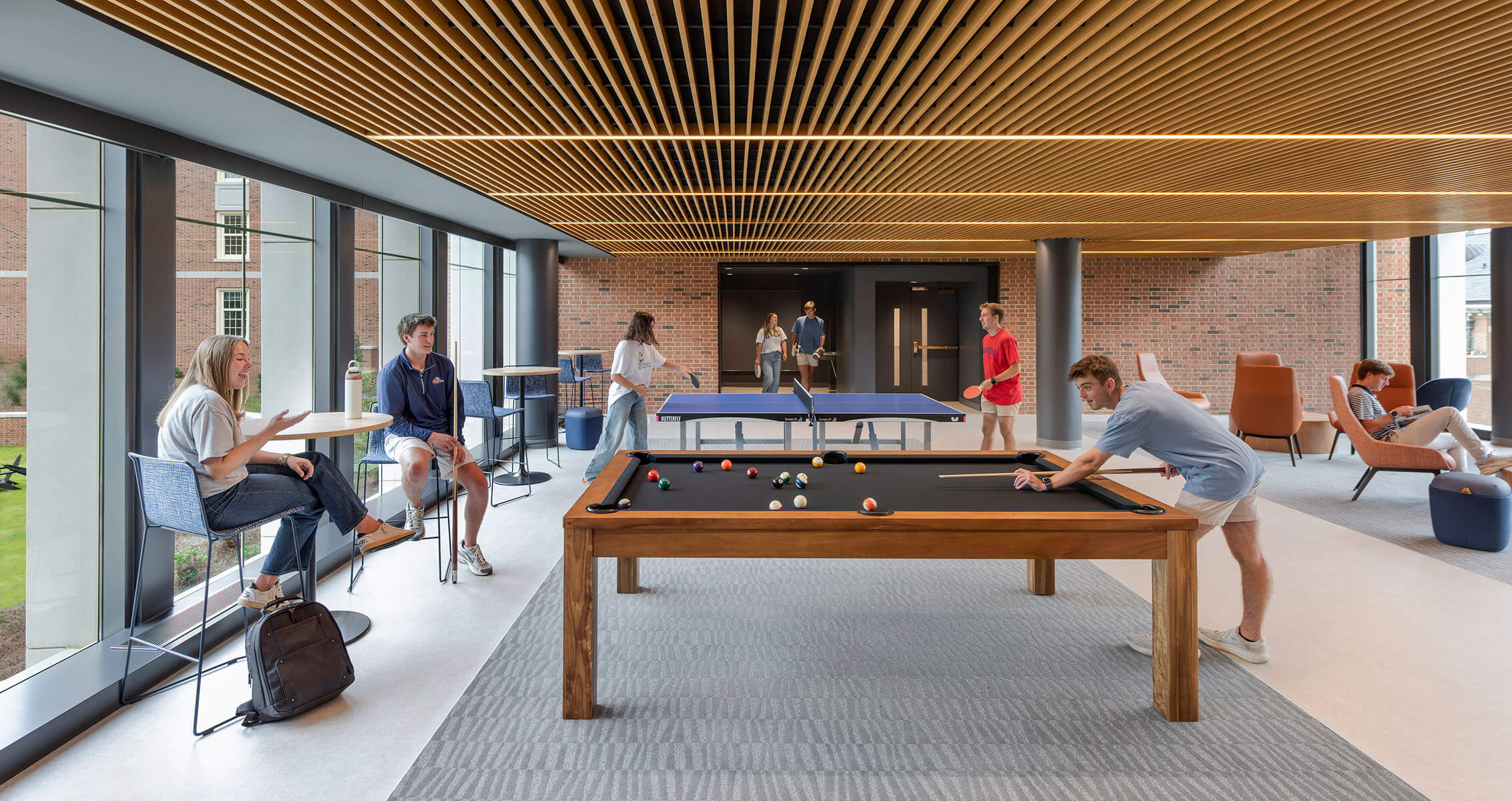 Students engage in leisure activities in a spacious lounge area featuring billiards and table tennis, with ample natural light and comfortable seating.