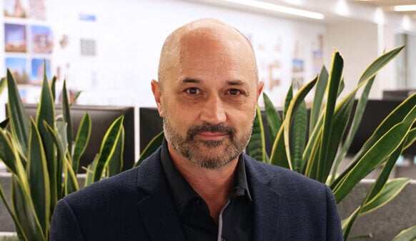 Portrait of a man in an office environment, featuring sleek furnishings and abundant greenery, highlighting balanced architectural design elements.