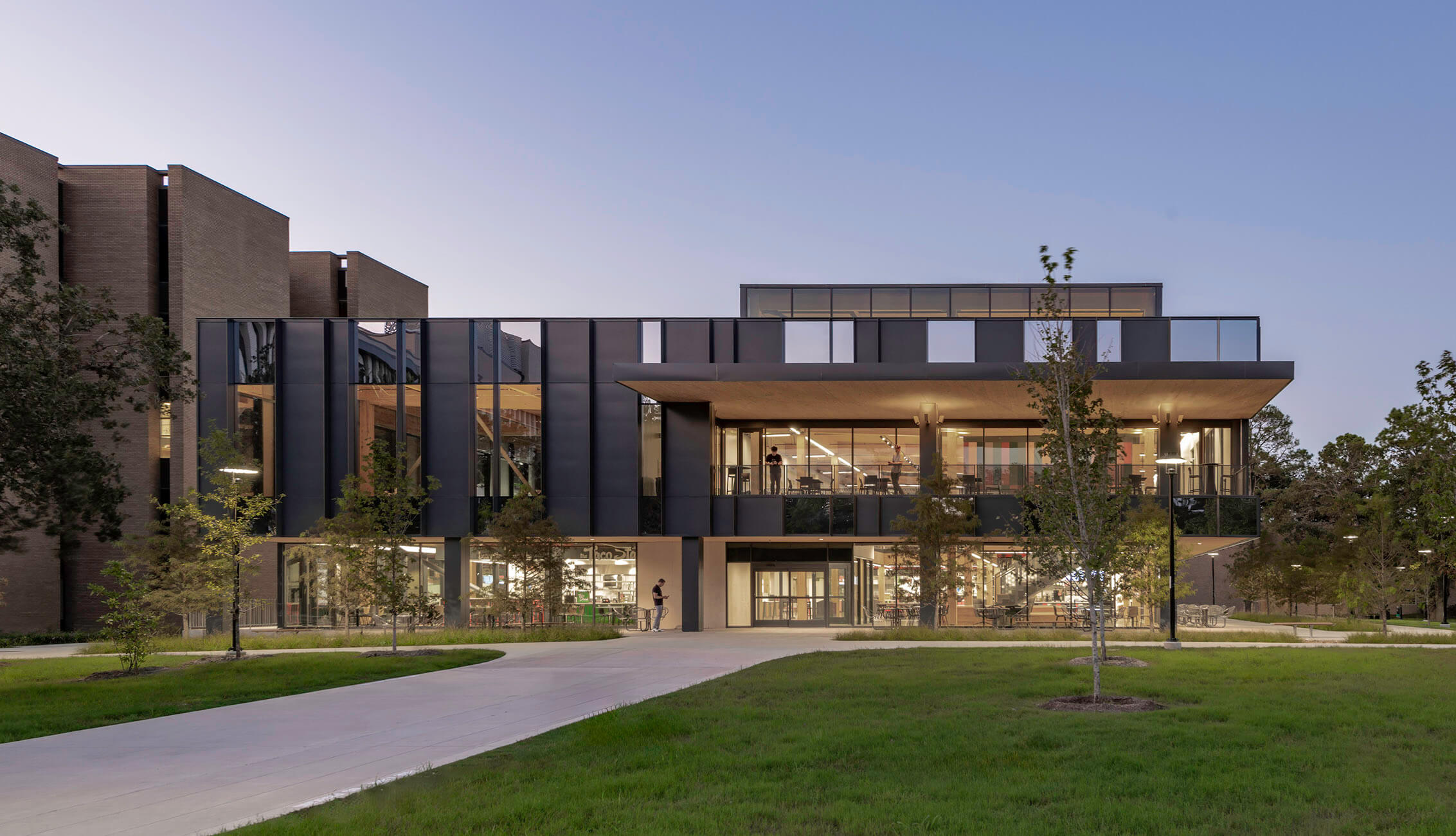 Newly designed building with large glass windows and landscaped lawn, featuring multiple levels and outdoor seating areas.