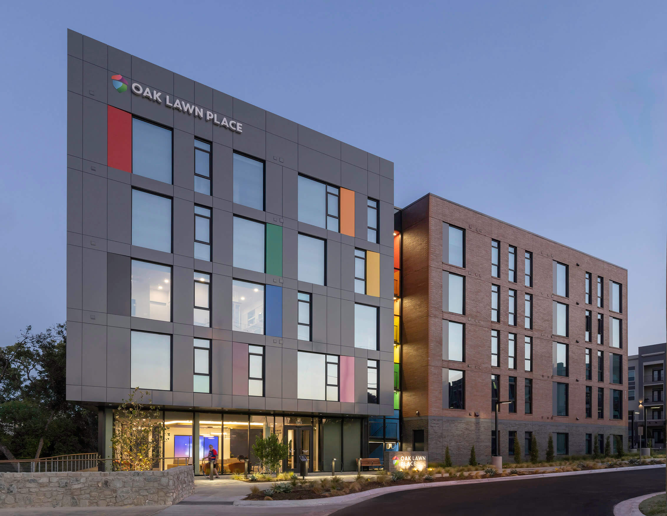 Exterior view of Oak Lawn Place, featuring a blend of brick and panel design with colorful accents, set against a twilight sky.