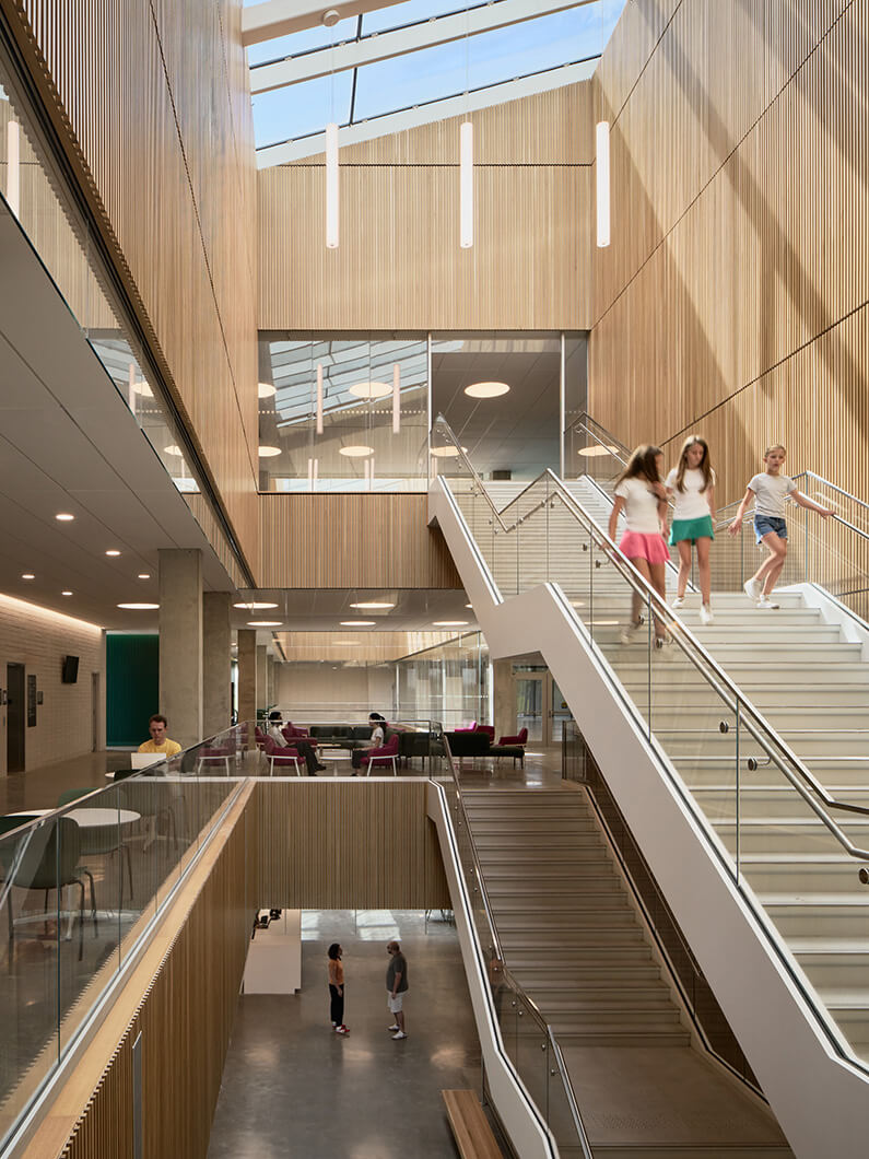 Interior view of a multi-level space with wooden walls, stairs, and people interacting in an open area with natural light.