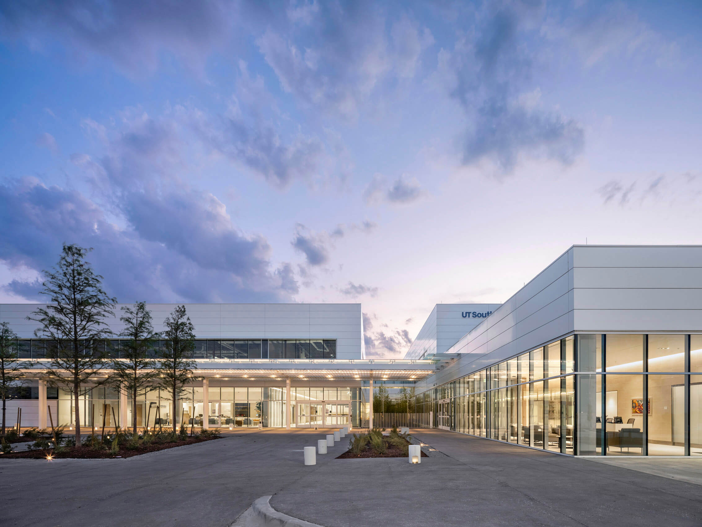 Exterior view of the UT Southwestern facility showcasing large glass windows, landscaped greenery, and a clear sky at dusk.