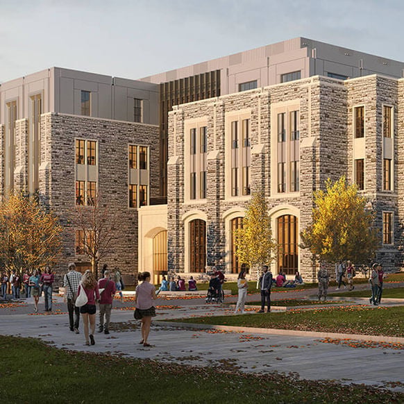 Students gather on campus near a stone building with large windows and trees, showcasing an active university environment.