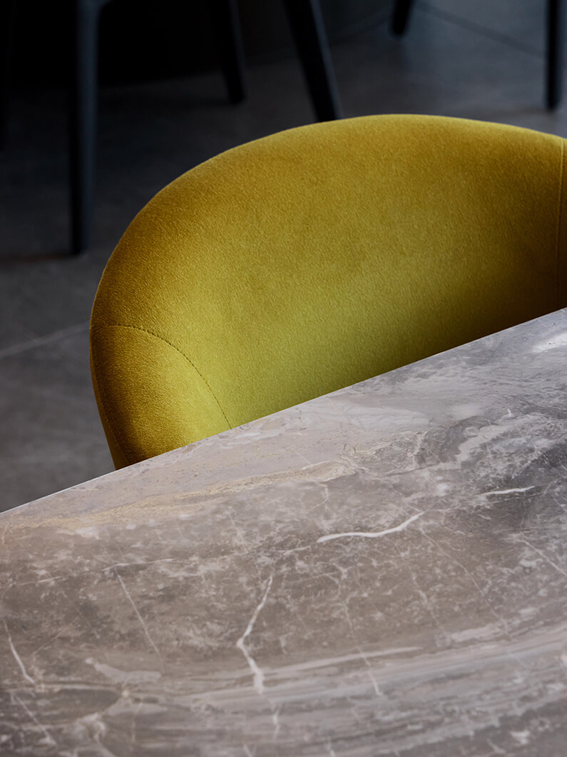 Detail of a round chartreuse chair beside a gray marble table, with a simple background of blurred seating.