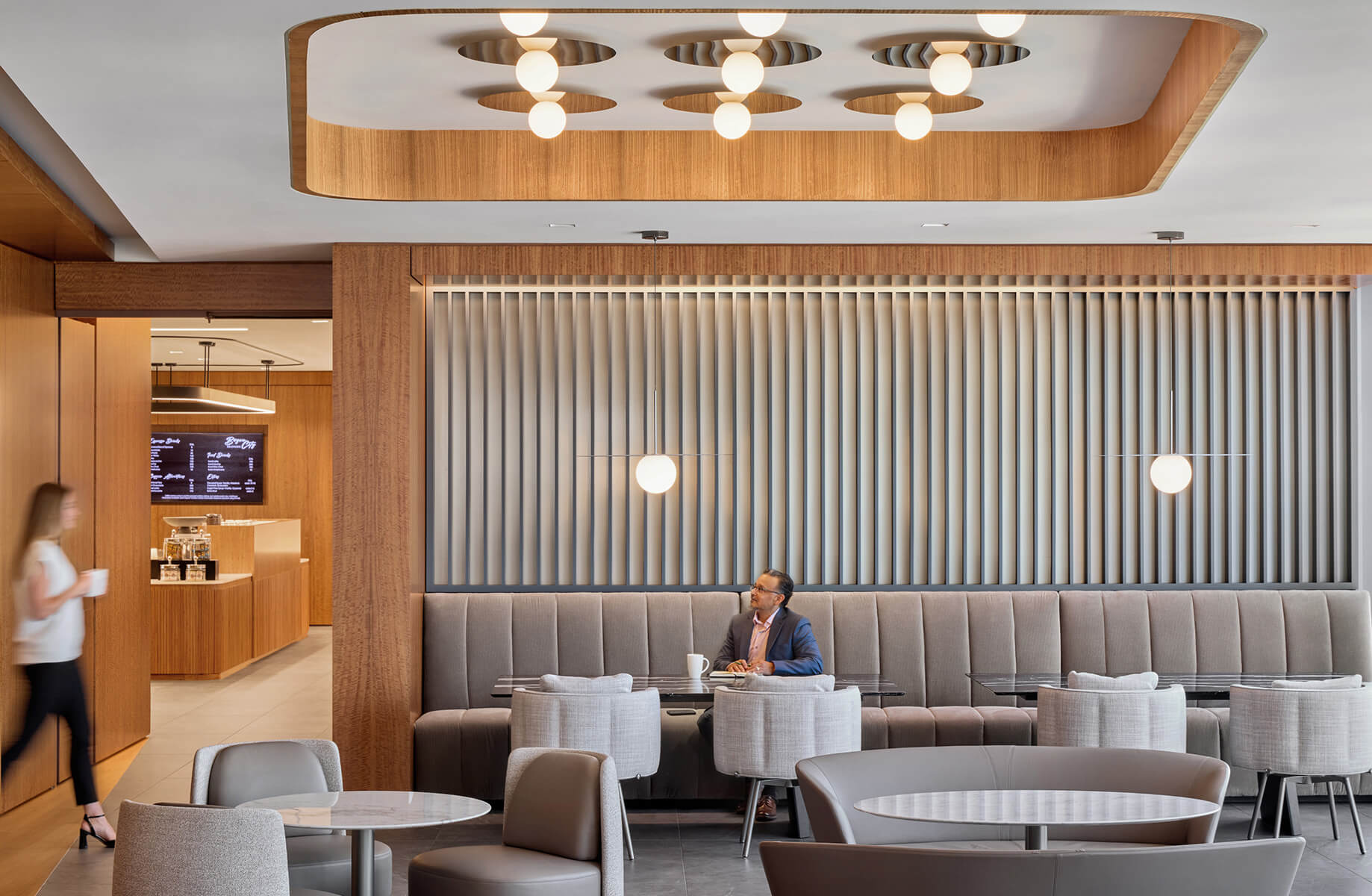 A spacious café interior featuring a man sitting at a table, surrounded by soft seating and warm wood accents, with a coffee menu in the background.