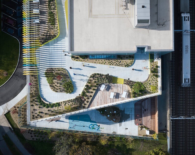 Aerial view of William E. Carter School's landscaped rooftop with pathways, seating areas, and greenery, adjacent to a train track. People walk through the space.