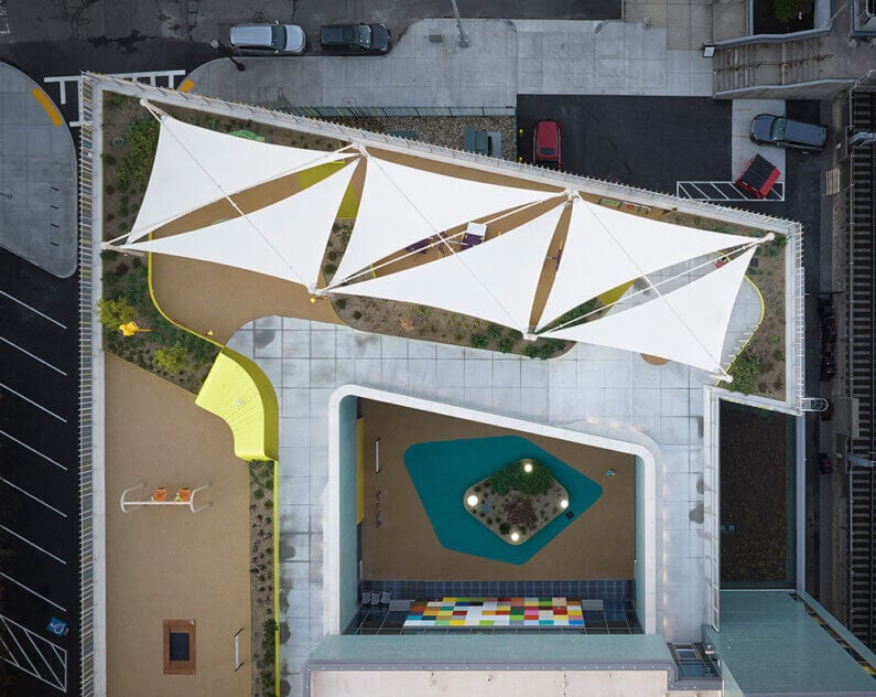 Aerial view William E. Carter School's rooftop playground with shade sails, colorful paths, and various landscaped areas designed for recreational use.