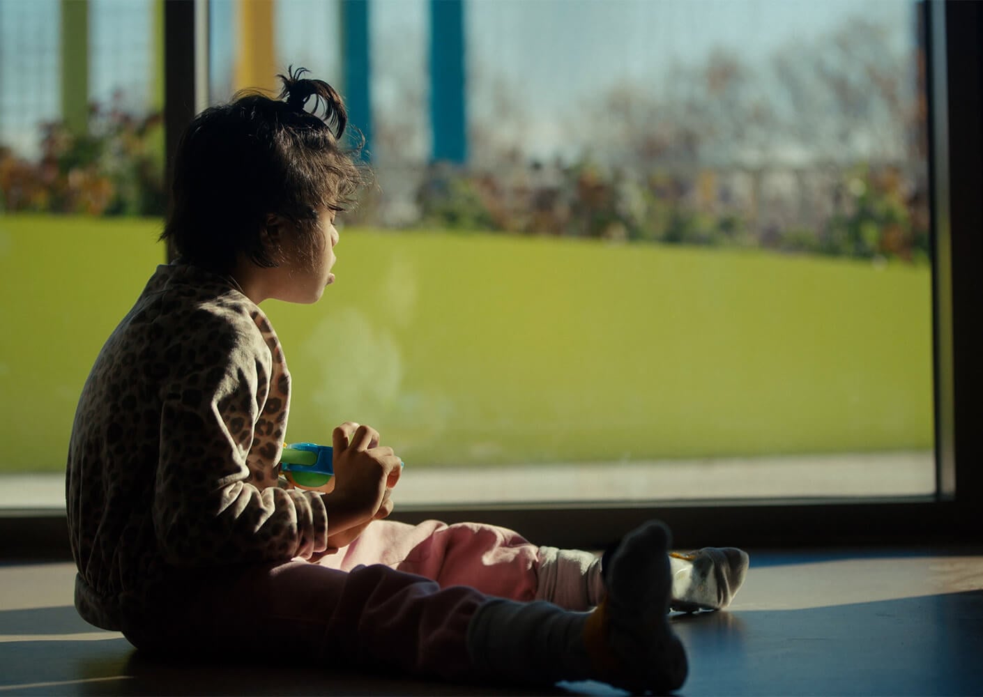 A child sitting by a window, looking outside to a colorful rooftop garden.