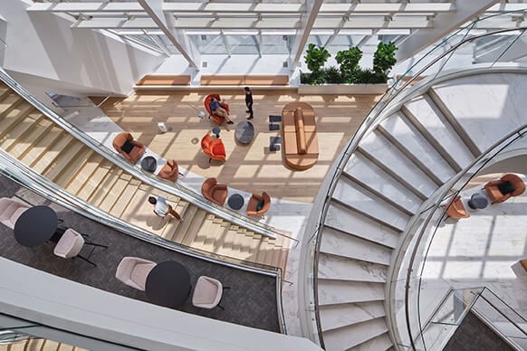 Open atrium view featuring a spiral staircase, seating areas, and greenery, promoting social interaction and accessibility in a spacious environment. 